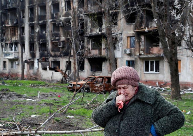 Starejša prebivalka Mariupolja pred uničeno stanovanjsko stavbo. FOTO: Alexander Ermochenko/Reuters
