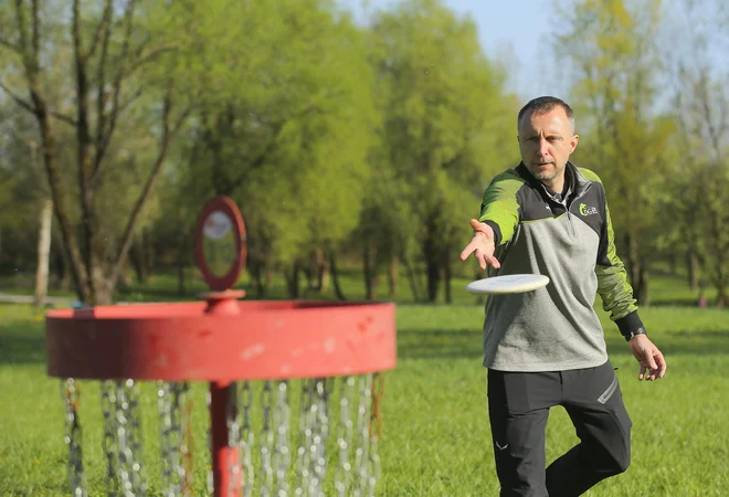 Aleksander Savnik, predsednik Disc golf kluba Ljubljana, potrpežljivo pokaže, kako vreči disk, da se zasliši tisti magični žvenket verig. FOTO: Jože Suhadolnik/Delo
