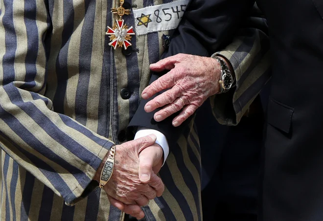 Poljski predsednik Andrzej Duda in Edward Mosberg, ki je preživel holokavst, se držita za roke pred »zidom smrti«. Gre za vsakoletni mednarodni Pohod živih po območju nekdanjega taborišča smrti Auschwitz v Oswiecimu na Poljskem. Foto: Kacper Pempel/Reuters