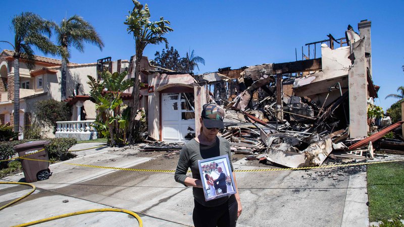 Fotografija: Lynn Morey stoji pred svojim požganim domom in drži portret nje in njenega moža Keitha Moreyja, ki ga je gasilec nezavestnega našel po požaru v Laguni Niguel v Kaliforniji. Nenaden in silovit požar, ki je v nekaj minutah zajel luksuzno enklavo v Kaliforniji in uničil več milijonov dolarjev vredne hiše, sta poslabšala veter in velikost nepremičnin. Požar, ki je izbruhnil 11. maja, se je hitro širil in zajel skupnost Laguna Niguel v bližini Los Angelesa. Okoli 1 000 domov je bilo evakuiranih, saj se je požar razširil na 80 hektarjev , uničil in poškodoval pa je okoli 30 nepremičnin. Foto: Apu Gomes/Afp
