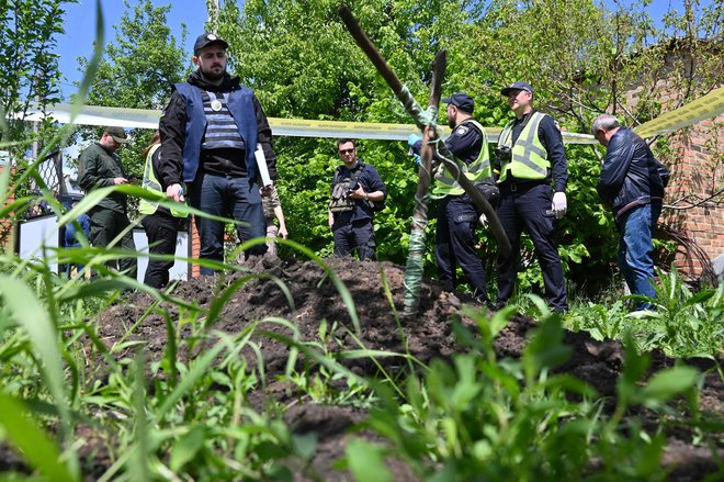 Ukrajinski policijski forenziki pri ekhumaciji trupla domnevne civilne žrtve, ki naj bi jo ruski vojak ustrelil v vasi Mala Rogan v bližini Harkova. FOTO: Sergey Bobok/AFP
