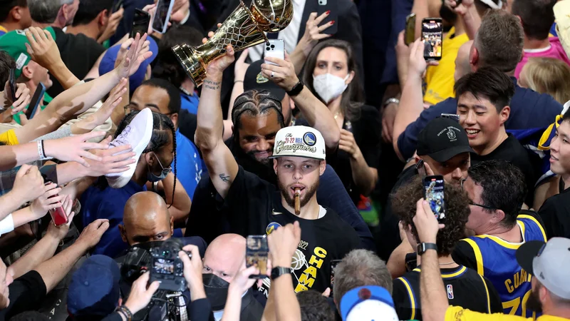 Fotografija: Stephen Curry z novo lovoriko in šampionsko cigaro, obkoljen z nepregledno množico. FOTO: Paul Rutherford/USA Today Sports