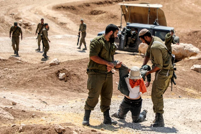 Izraelski vojaki so pridržali protestnika, ki se je udeležil demonstracij palestinskih aktivistov proti izselitvi palestinskih vasi, da bi naredili prostor za izraelsko vojaško vadbeno območje, na južnem gričevju Yatta, južno od mesta Hebron na okupiranem Zahodnem bregu. FOTO: Mosab Shawer/AFP