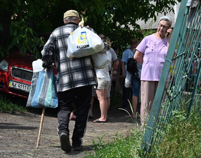 Starejši moški nosi vrečke s humanitarno pomočjo, ki so jih razdelili prostovoljci v mestu Lyubotyn v regiji Harkov. FOTO: Sergey Bobok/AFP
