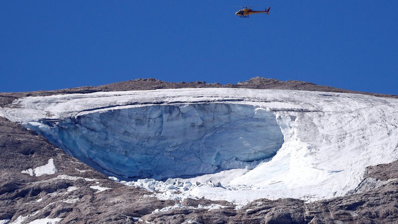Fotografija: Reševalni helikopter med iskanjem pogrešanih v sobotni nesreči na ledeniku na gori Marmolada. FOTO: Guglielmo Mangiapane/ Reuters

