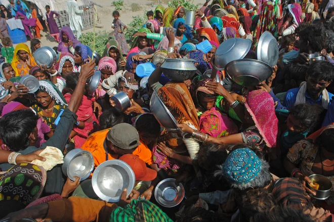 Notranje razseljeni Pakistanci se zbirajo, da bi prejeli brezplačno hrano v bližini svojega začasnega taborišča v provinci Sindh, ki so jo prizadele poplave epskih razsežnosti. Foto: Afp