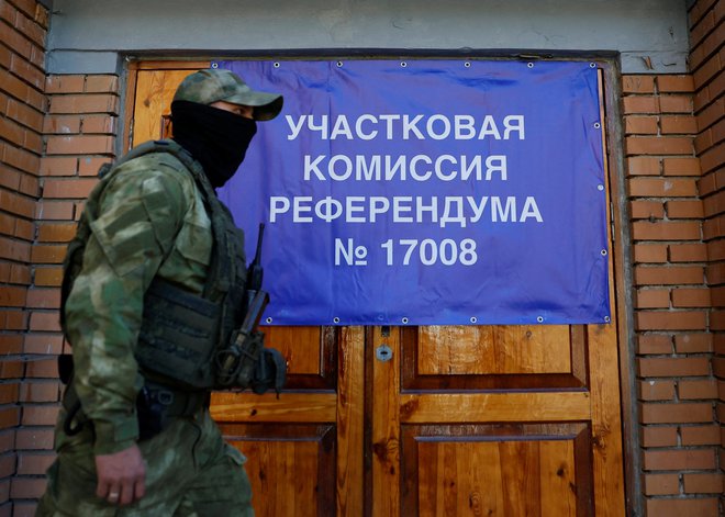 Pripadnik samooklicane Ljudske republike Doneck ob transparentu o referendumu o priključitvi Rusiji. FOTO: Aleksander Ermočenko/Reuters
