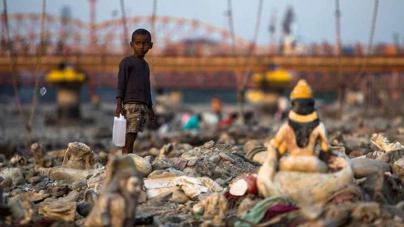 Fotografija: Indijski deček s kantico vode hodi med po onesnaženi plaži ob strugi reke Ganges v Haridwarju. Foto: Xavier Galiana/Afp