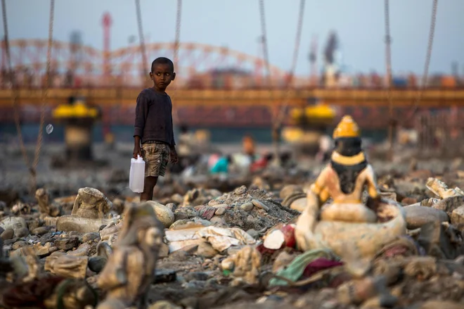 Indijski deček s kantico vode hodi med po onesnaženi plaži ob strugi reke Ganges v Haridwarju. Foto: Xavier Galiana/Afp
