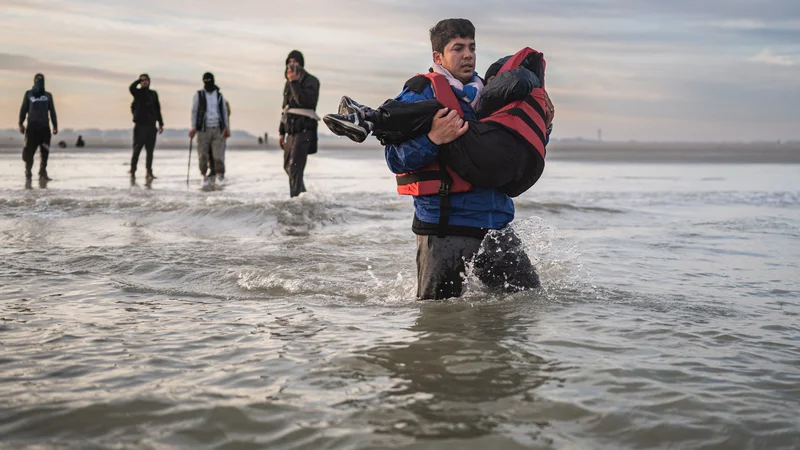 Fotografija: Migrant nosi otroka na tihotapsko ladjo pri mestu Dunkerque na severu Francije. Trenja med evropskimi državami pri azilnih in migracijskih vprašanjih ostajajo bolj ali manj enaka kot po izbruhu velike begunske krize leta 2015. FOTO: Sameer Al-doumy/AFP