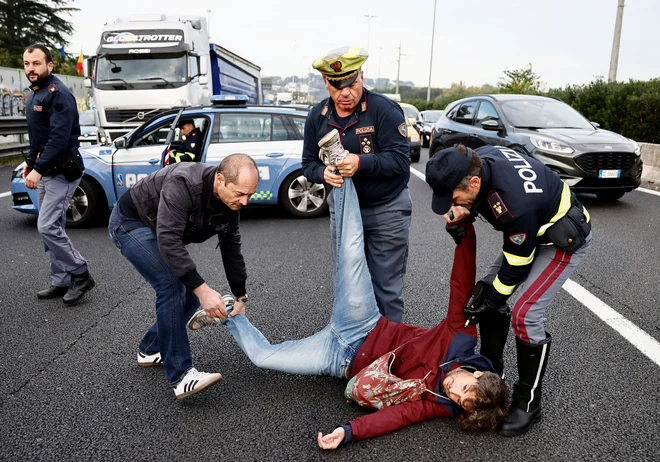 Policisti se trudijo odstraniti moškega iz ceste v Rimu, medtem ko italijanski podnebni aktivisti »Ultima Generazione« blokirajo avtocesto in opozarjajo na potrebo po boju proti podnebni krizi. Foto: Yara Nardi/Reuters