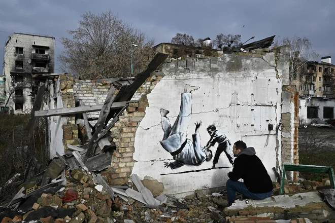 Ulični umetnik Banksy je na svojem uradnem profilu na Instagramu objavil posnetek najnovejšega dela, ki ga je ustvaril na pročelju poškodovane stavbe v Ukrajini. V Kijevu je upodobljen otrok, ki v judoističnem dvoboju zavihti odraslega moškega, ki spominja na Vladimirja Putina, za katerega je znano, da ima črni pas v judu. Foto: Genya Savilov/Afp