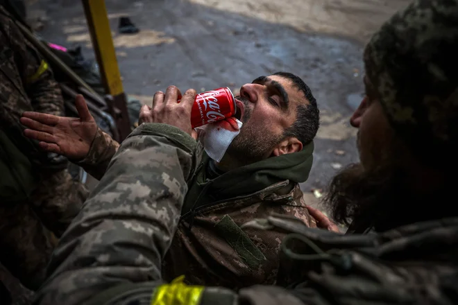 Ukrajinski vojak pomaga ranjenemu tovarišu piti med evakuacijo v mobilni bolnišnici v okolici Bakhmuta v regiji Doneck med rusko invazijo na Ukrajino. Foto: Anatolij Stepanov/Afp