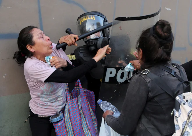 Ženski se upirata policistu med protestom v Limi, na katerem zahtevajo razpustitev kongresa in demokratične volitve, ne pa priznanje Dine Boluarte za novo predsednico Peruja po odstavitvi perujskega predsednika Pedra Castilla. FOTO: Sebastian Castaneda/Reuters