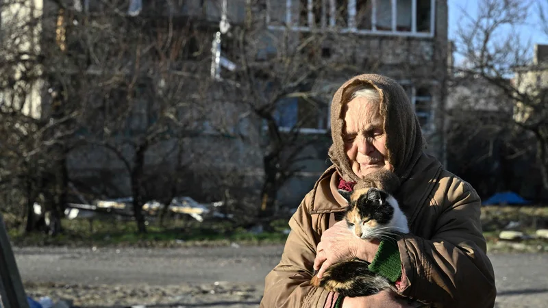Fotografija: 80-letna domačinka Galyna drži mačko pred poškodovano stavbo v mestu Lyman v oblegani regiji Doneck, v kateri živi brez elektrike, vode in ogrevanja. Foto: Genya Savilov/Afp