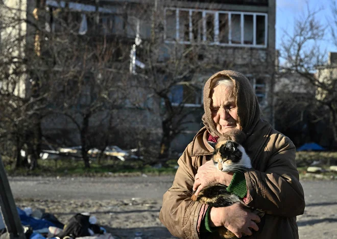 80-letna domačinka Galyna drži mačko pred poškodovano stavbo v mestu Lyman v oblegani regiji Doneck, v kateri živi brez elektrike, vode in ogrevanja. Foto: Genya Savilov/Afp