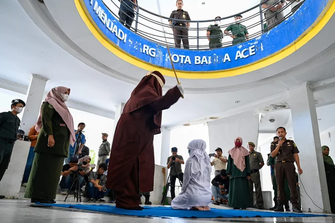 V indonezijskem mestu Banda Aceh šeriatski policist s palico javno kaznuje žensko, ker jo je ujel v bližini moškega. Foto: Chaideer Mahyuddin/Afp