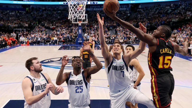 Fotografija: Clint Capela prodira pod koš, ustavljajo ga Dwight Powell, Reggie Bullock in Luka Dončić (z leve) med zadnjo četrtino dvoboja Dallasa in Atlante v dvorani American Airlines Center. FOTO: Tom Pennington/AFP