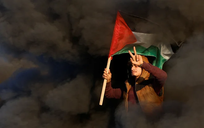 Palestinec drži palestinsko zastavo med spopadi z izraelskimi silami v bližini meje med Izraelom in Gazo vzhodno od mesta Gaza. Foto: Mohammed Salem/Reuters