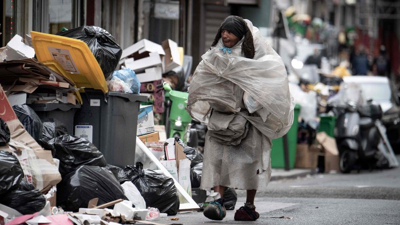 Fotografija: Brezdomec, pokrit s plastičnimi vrečkami, hodi mimo smeti, ki so se kopičijo na ulicah Pariza, saj delavci komunalnih podjetij že od 6. marca stavkajo proti predlagani pokojninski reformi francoske vlade. Foto: Alain Jocard/Afp
