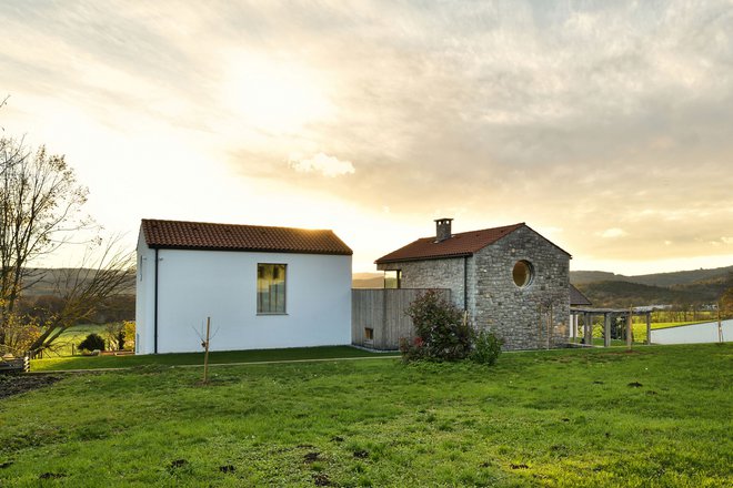 Hiša za mlado družino na robu kraške vasi je oblikovana v treh volumnih. Stara hiša (belo ometana) je z novo kamnito povezana s teraso. FOTO: Matej Lozar