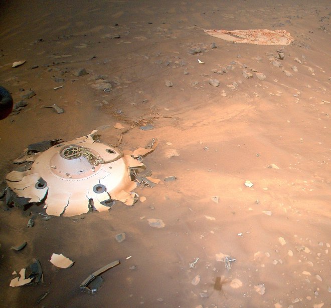 Zaradi takšnih posnetkov je Ingenuity za znanstvenike zelo dragocen: 19. aprila lani je namreč z višine osmih metrov posnel ščit kapsule, v kateri je bil rover, in padalo. Posnetek so si želeli inženirji, ki že pripravljajo prihodnjo odpravo na Mars, da dobijo nov vpogled, kako delujejo pristajalni sistemi. Foto Nasa/JPL-Caltech