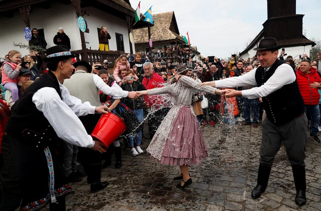 Ženska v tradicionalnih oblačilih se odzove, ko jo moški polijejo z vodo med tradicionalnim praznovanjem velike noči v Holloku na Madžarskem. Foto: Bernadett Szabo/Reuters
