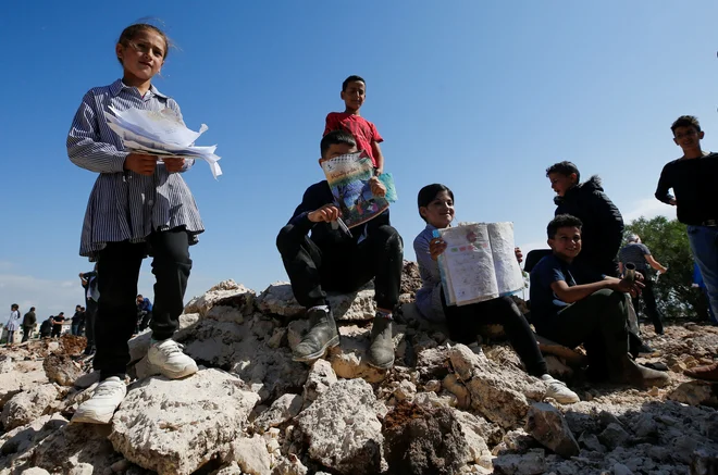 Palestinski šolarji z poškodovanimi učbeniki po izraelskem rušenju šole. FOTO: Mussa Issa Qawasma/Reuters