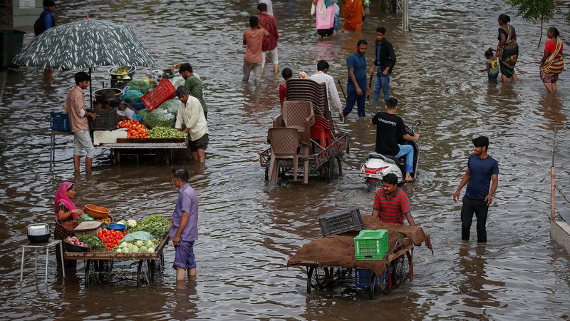 Fotografija: Indijci kupujejo zelenjavo pri uličnih prodajalcih, medtem ko se drugi prebijajo skozi poplavljeno cesto po močnem deževju v Ahmedabadu. Foto: Amit Dave/Reuters