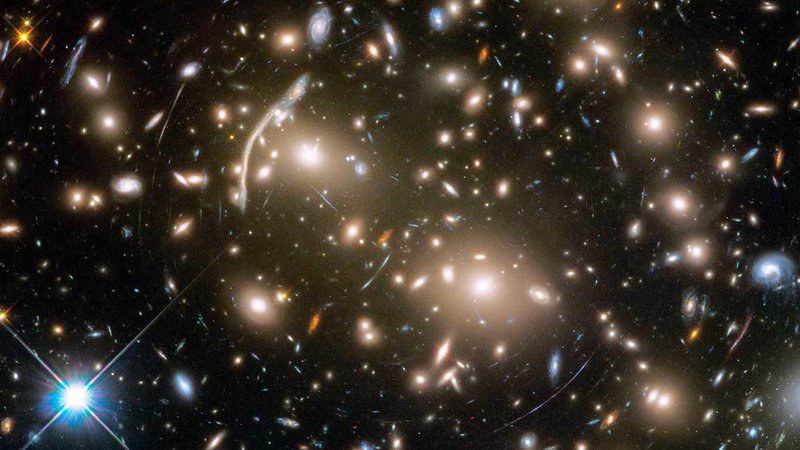 Fotografija: Jata galaksij Abell 370, ki je oddaljena približno štiri milijarde svetlobnih let, vsebuje osupljivo paleto več sto galaksij, povezanih z medsebojno gravitacijo. Med galaksijami so skrivnostni loki modre svetlobe, ki so pravzaprav popačene slike oddaljenih galaksij za jato. FOTO: Nasa/Esa