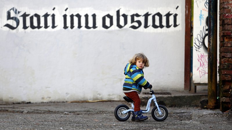 Fotografija: Otrok na kolesu pred napisom Stati inu obstati. FOTO: Matej Družnik/Delo