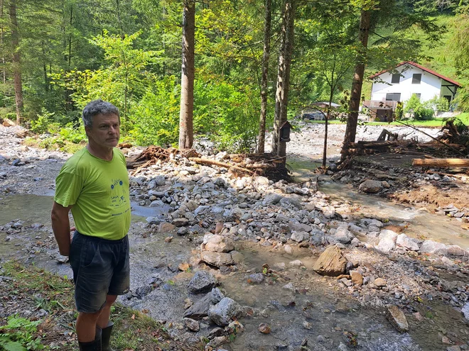 Albert Kolar je še naprej odrezan od sveta, njegova hiša je v ozadju. Cesta je bila prej tu, ob njem, zdaj pa je po novem tam še ena struga. FOTO: Špela Kuralt/Delo