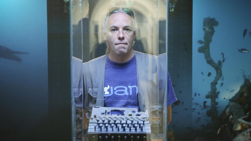 Fotografija: Aleš Jelinčič pred stekleno vitrino, v kateri je na ogled Enigma. FOTO: Jože Suhadolnik/Delo