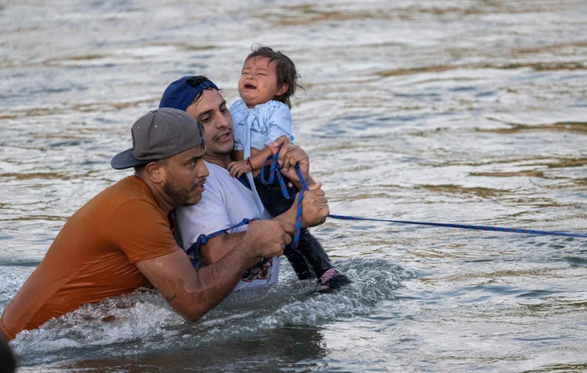 29-letni Yonder Urbina iz Venezuele, ki drži enoletno Olgo iz Mehike, in 30-letni Oskeivys Gonzales iz Venezuele vlečeta za vrv, ki jo držijo drugi migranti, ko prečkata globlji del reke Rio Grande do Eagle Passa v Teksasu. Foto: Andrew Caballero-reynolds/Afp