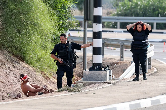 Palestinski zapornik z zavezanimi očmi se pogovarja s članom izraelskih varnostnih sil na meji z Gazo blizu južnega izraelskega mesta Aškelon. Izraelski varnostni svet je uradno razglasil vojno stanje, kar omogoča daljnosežne vojaške korake po napadih palestinskega gibanja Hamas. Skupno je na obeh straneh že več kot 1.100 žrtev. Foto: Jack Guez/Afp