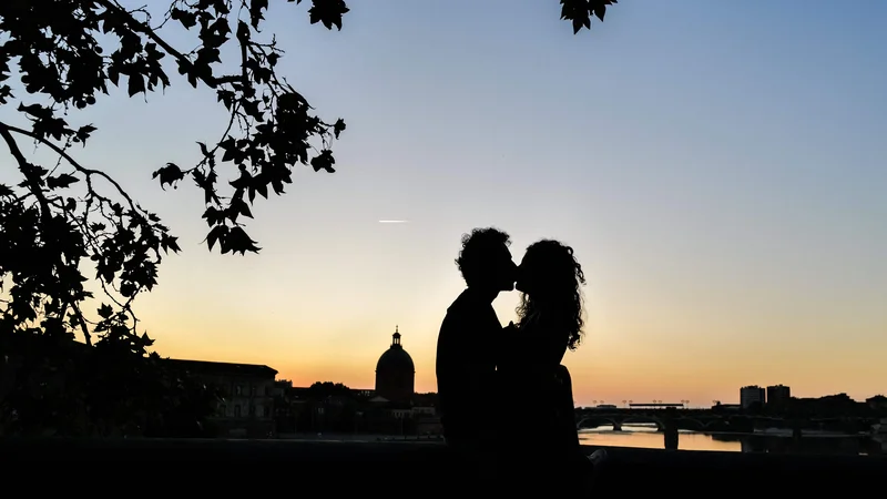 Fotografija: Par se poljublja ob sončnem zahodu ob bregu reke Garone v Toulusu, v ozadju pa je znamenitost Dome de la Grave. Foto: Charly Triballeau/Afp