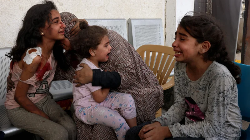 Fotografija: Ženska tolaži ranjena palestinska dekleta, ki čakajo na pregled v bolnišnici v mestu Rafa na jugu Gaze, medtem ko se spopadi med Izraelom in gibanjem Hamas nadaljujejo že sedmi dan zapored. Foto: Said Khatib/Afp