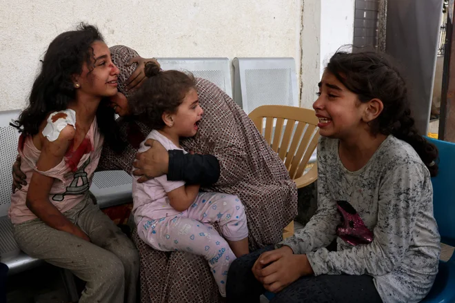 Ženska tolaži ranjena palestinska dekleta, ki čakajo na pregled v bolnišnici v mestu Rafa na jugu Gaze, medtem ko se spopadi med Izraelom in gibanjem Hamas nadaljujejo že sedmi dan zapored. Foto: Said Khatib/Afp