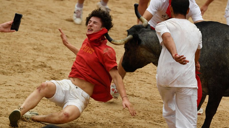 Fotografija: Julij 2023. Boleč utrinek iz festivala San Fermin v Pamploni na severu Španije. Tisoče ljudi se vsako leto udeleži tedenskega festivala in njegovega znamenitega »encierra« (tek pred biki). Vsak dan ob 8.00 izpustijo šest bikov, ki tečejo iz svoje ograde do arene po ozkih ulicah starega mesta na 850 metrov dolgi progi, medtem ko se tekači pred njimi trudijo ostati blizu bikov, ne da bi padli ali se podrli. Foto: Miguel Riopa/Afp