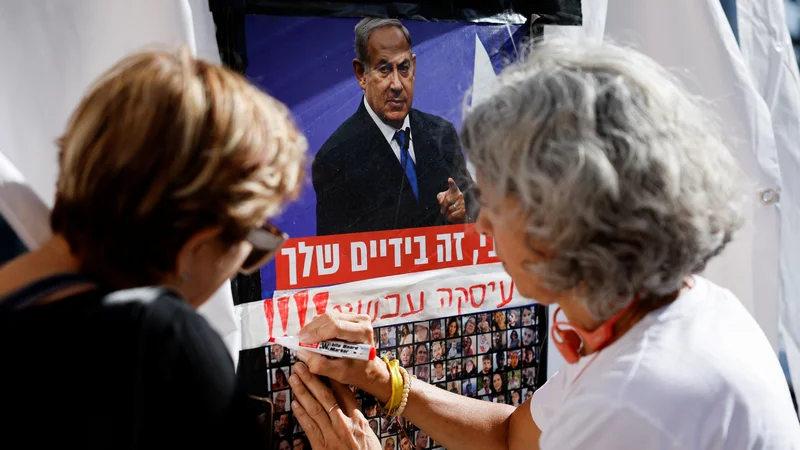 Fotografija: Ženska je na plakat s podobo Netanjahuja in fotografijami zajetih talcev zapisala: vse je v tvojih rokah. FOTO: Amir Cohen/Reuters