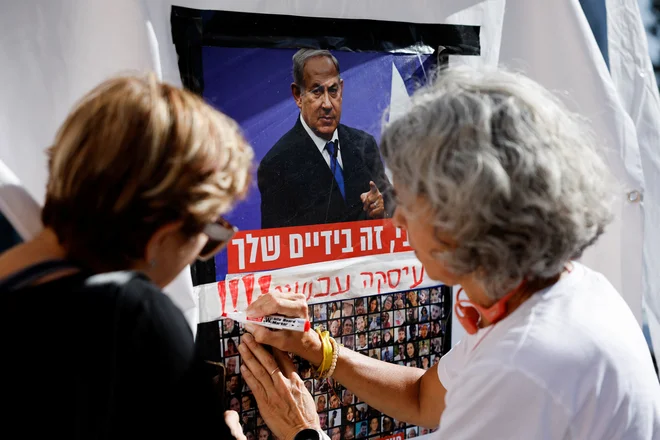 Ženska je na plakat s podobo Netanjahuja in fotografijami zajetih talcev zapisala: vse je v tvojih rokah. FOTO: Amir Cohen/Reuters