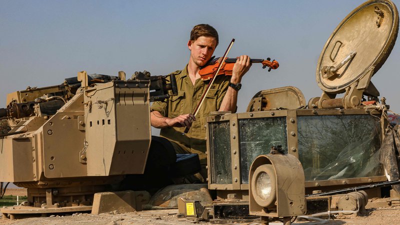 Fotografija: Na jugu Izraela blizu meje z območjem Gaze, izraelski vojak igra na violino na tanku. Foto: Menahem Kahana/Afp