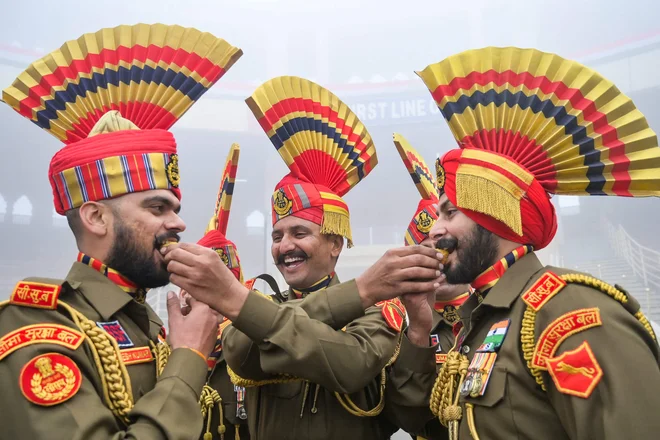 Vojaki indijskih obmejnih varnostnih sil (BSF) si med praznovanjem dneva republike na indijsko-pakistanskem mejnem prehodu Wagah, približno 35 km od Amritsarja, med seboj ponujajo sladkarije. Foto: Narinder Nanu/Afp