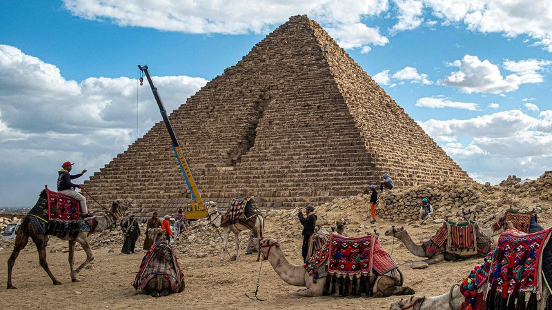 Fotografija: V Giizi kamele počivajo ob Menkaurjevi piramidi, zgrajeni v 26. stoletju pred našim štetjem. Mostafa Waziri, vodja egipčanskega vrhovnega sveta za starine, je v videoposnetku na Facebooku, pokazal, kako delavci postavljajo granitne bloke na osnovo piramide, in ga označil za projekt stoletja. Ko je bila piramida prvotno zgrajena, je bila obdana z granitom, vendar je sčasoma izgubila del obloge. Cilj prenove je z obnovo granitne plasti povrniti prvotni arhitekturni slog. Foto: Khaled Desouki/Afp