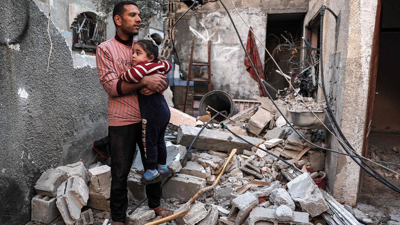 Fotografija: Palestinec drži v rokah deklico, stoječ na ruševinah, ki jih je povzročilo izraelsko bombardiranje. FOTO: Said Khatib/AFP
