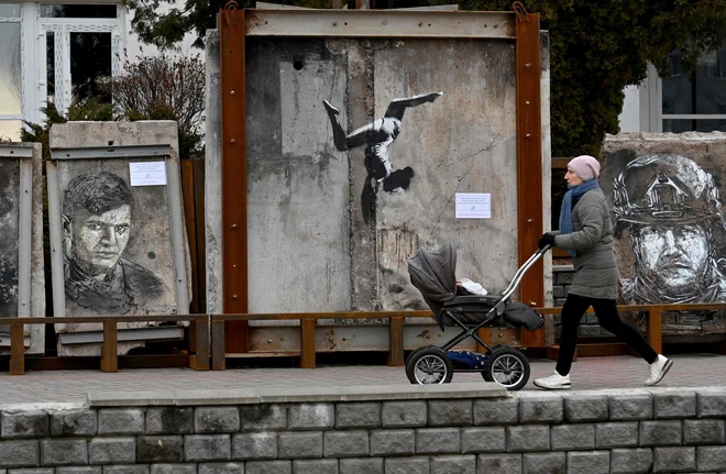 Ženska gre mimo umetnine angleškega uličnega umetnika Banksyja, ki je del razstave grafitov na prostem na osrednjem trgu Borodjanka v regiji Kijev. Umetnine mednarodnih in ukrajinskih umetnikov, ki so slikali na ruševinah porušenih stavb med rusko invazijo na Ukrajino, so lahko razstavili šele, ko so bile stavbe pozrušene. Foto: Sergei Supinsky/Afp