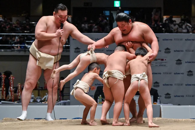 Jokozuna, upokojeni sumoborec mongolskega rodu , ki zdaj nosi ime Miyagino, opazuje, kako poskušajo otroci izriniti japonskega sumoborca Hakuoha med uro sumoborbe za mlade, ob robu 14. pokala Hakuho, namenjenega mladim sumoborcem iz osnovnih in srednjih šol, v tokijski areni Kokugikani. Foto: Richard A. Brooks/Afp