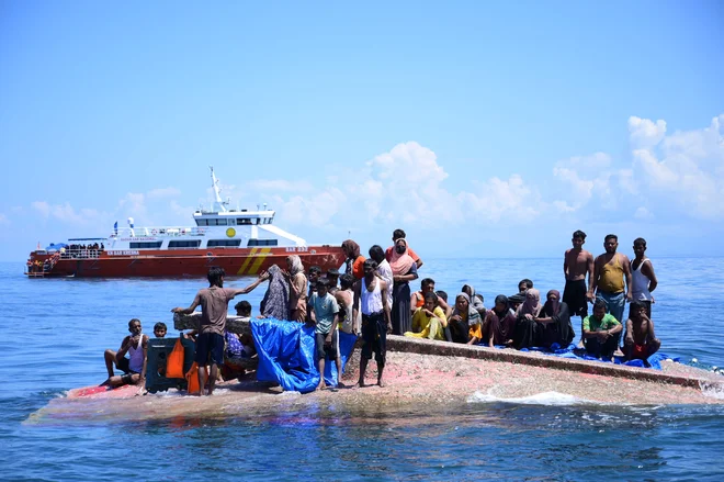 Rohinga begunci čakajo na rešitev iz trupa njihovega prevrnjenega čolna, ko se plovilo Nacionalne agencije za iskanje in reševanje približuje vodam približno 16 navtičnih milj od zahodnega Aceha. Indonezijske oblasti so rešile najmanj 69 beguncev, ki so bili tedne na morju in so jih 21. marca peljali na obalo, potem ko se je dan prej prevrnilo njihovo plovilo. Foto: Zahlul Akbar/Afp