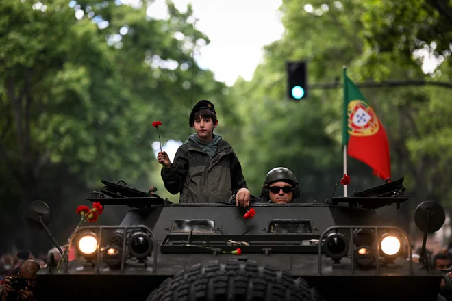 Otrok z rdečim nageljnom in nekdanji vojak na vrhu vojaškega vozila Chaimite, ki sodeluje na shodu na Avenidi da Liberdade v Lizboni. Portugalska obeležuje 50. obletnico revolucije nageljev, vojaškega udara, ki je končal najdlje trajajočo diktaturo v Evropi in 13 let trajajoče kolonialne vojne v Afriki. Foto: Patricia De Melo Moreira/Afp