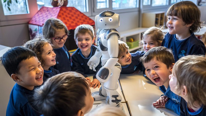 Fotografija: Predšolski otroci se v vrtcu v univerzitetnem kampusu Švicarskega zveznega inštituta za tehnologijo v Lozani družijo z izobraževalnim in interaktivnim robotom Nao. Nao je od novega leta redni obiskovalec vrtca Nanosphere. V krogu na tleh vrtca mladi navdušeno poslušajo Naove modrosti, ko prijazni robot z drugega planeta odgovarja na njihova vprašanja o žirafah in brokoliju. Foto: Fabrice Coffrini Afp